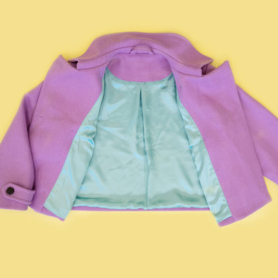 A lavender purple cropped jacket with a shiny mint green satin lining, laid flat against a solid yellow background.